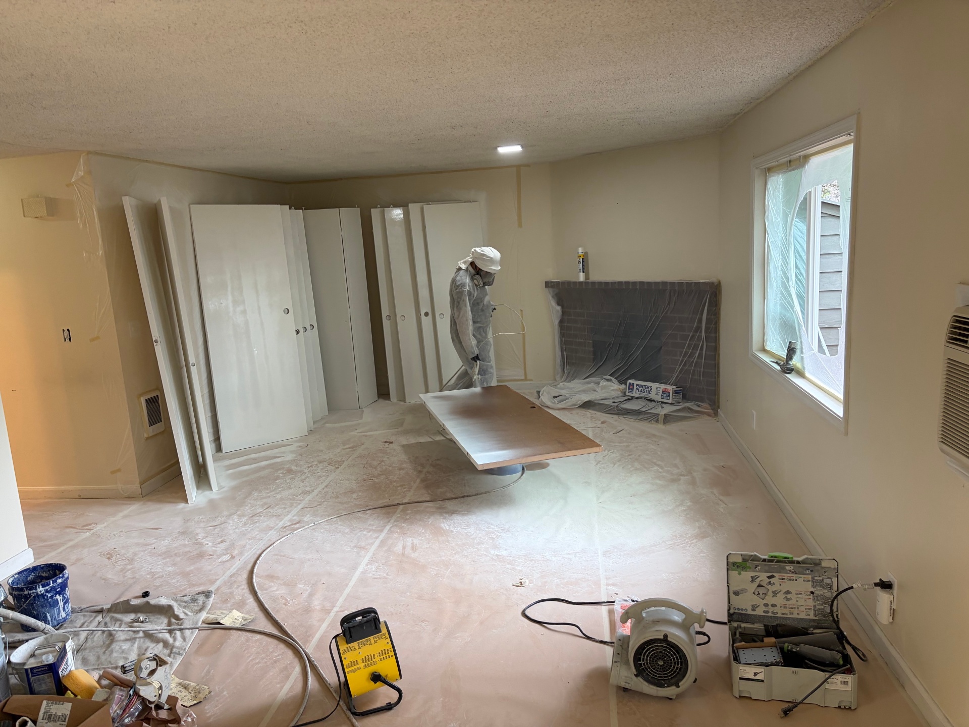 Image Home Renovations painter spray-applying white enamel finish to cabinet and interior doors inside a Portland Metro condo
