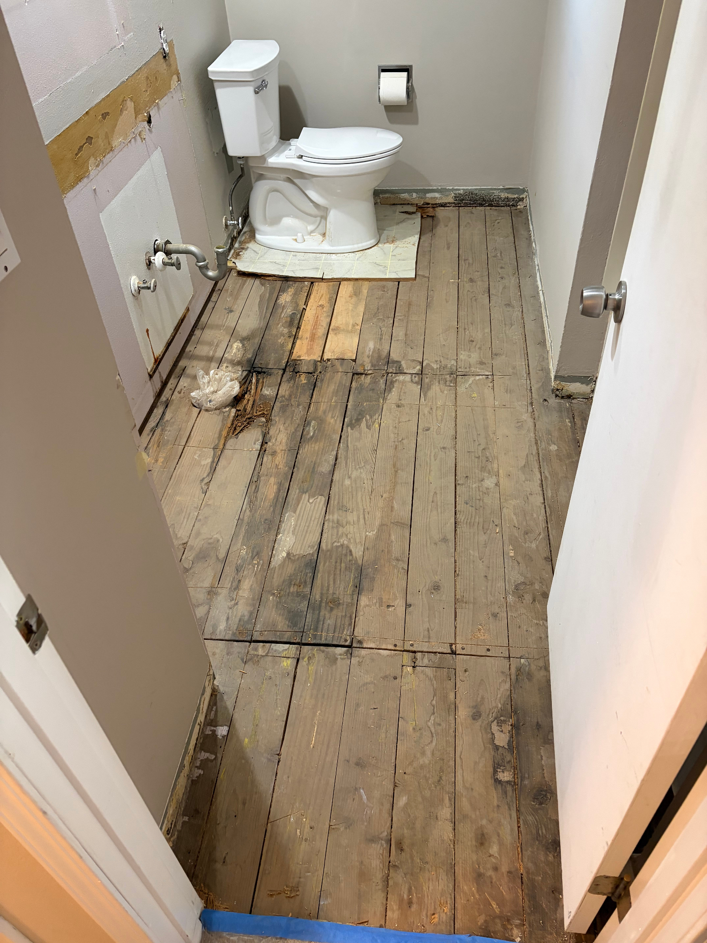 Original 1960s tongue-and-groove subfloor showing water damage before partial replacement and sistering